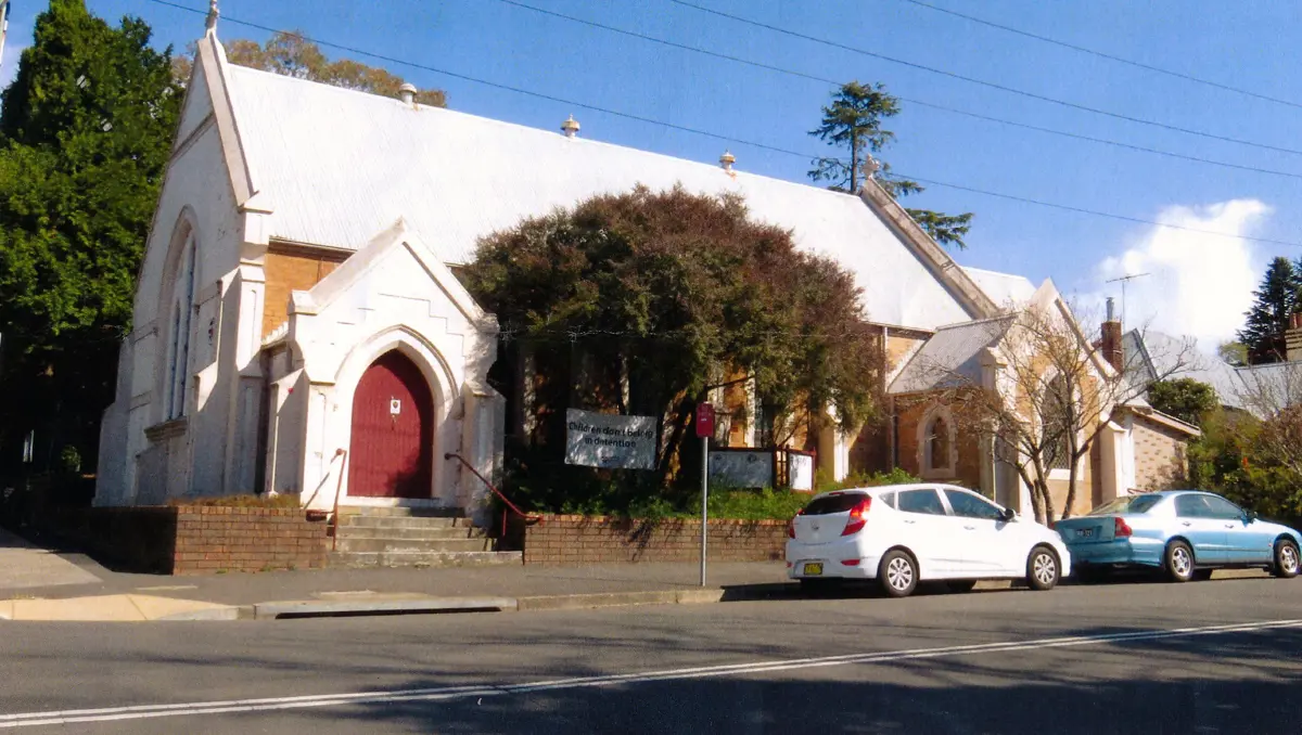 Front of Leura Uniting Church: a white gabled church with a red arched door and brick front fence